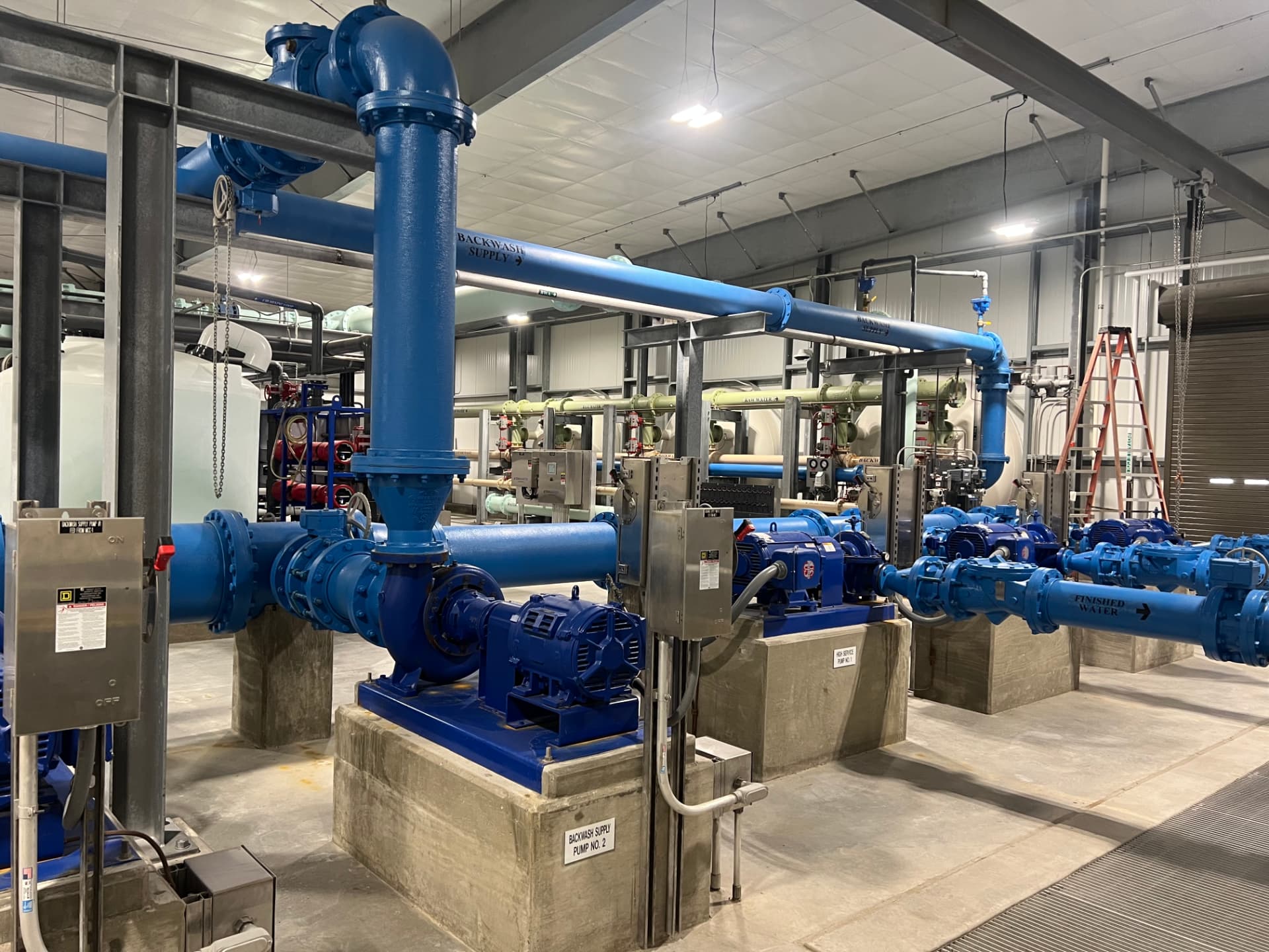 Interior of a water treatment plant showing finished-water and backwash pumps, motors, and blue piping